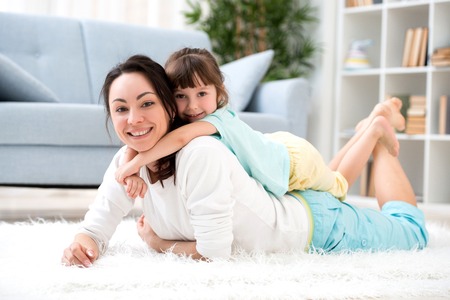 Happy loving family. Beautiful mother and little daughter have fun, play in the room on the floor, hug, smile and fool aroundの写真素材