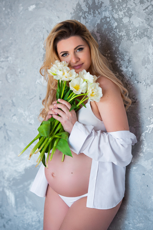 Beautiful young pregnant blonde woman love flowers white tulips. Spring mood, freshness, women's Day, health and beautiful pregnancy.の写真素材