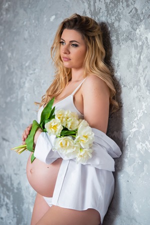 Beautiful young pregnant blonde woman love flowers white tulips. Spring mood, freshness, women's Day, health and beautiful pregnancy.の写真素材