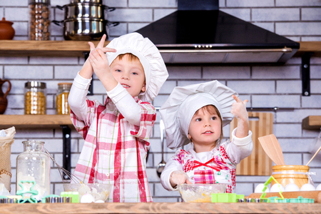 Children a boy and a girl knead a dough of flour and eggs and prepare delicious gingerbread and cookies in the kitchen.の写真素材