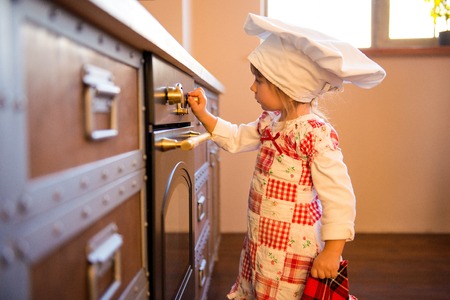 Girl in chef's hat is putting gingerbread cookies in the oven.の写真素材