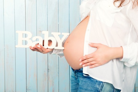Close-up. Woman holding a sign the word baby on the background of a pregnant tummy.