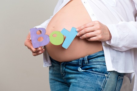 Close-up. Woman holding a sign the word boy on the background of a pregnant tummy.の写真素材