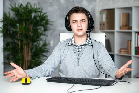A teenager boy in headphones playing computer games at pc at home in the interior in front of a computer monitor.の写真素材