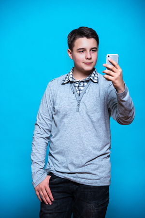 Boy schoolboy student teenager with a mobile phone in hand isolated on blue background.の写真素材