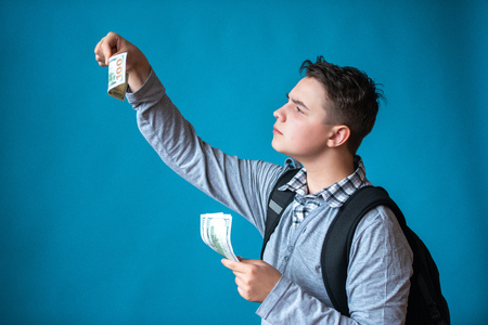 Cash loan, first easy money and spending money. Boy teenager holds in the hands money and checks authentic or fake bills. Earnings or winnings online.の写真素材