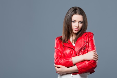 Fashionable style, fashion women's clothing, color combination. Beautiful brunette girl in white dress and red leather jacket isolated gray background.の写真素材