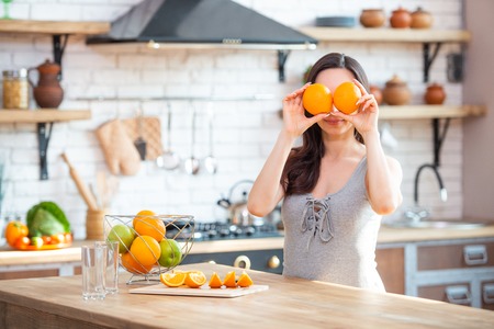 sporty young woman is cutting fresh orange for fruit juice in the kitchen. Horizontal indoors shot.の写真素材