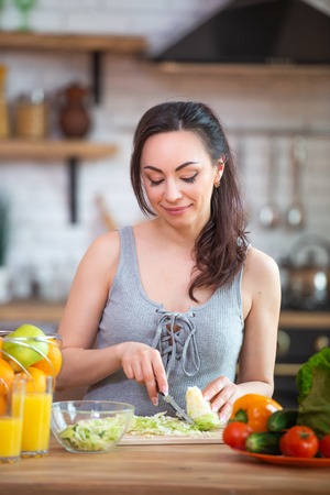 Pretty young woman cutting vegetables salad in the kitchen.