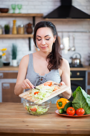 Pretty young woman cutting vegetables salad in the kitchen.の写真素材