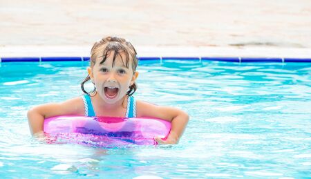 Little girl lying in swimming pool learning to swim on inflatable circle. Summer holidays, heat and...