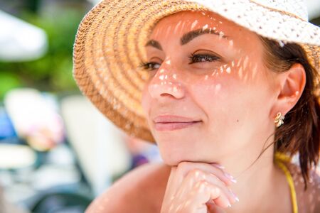 Brunette girl in a straw hat at the sea. Close-up portrait of a woman. Three quarters profile.