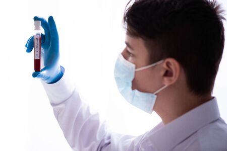 Test tube in male hand close up, doctor in medical mask holding a vial with red liquid. Concept of blood sample, coronavirus diagnostic, medical research.の写真素材