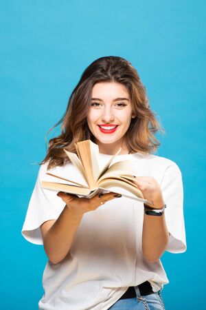 Girl holds and leafs a book in her hands on a blue background. The concept of education, knowledge, library, exam preparation.の写真素材