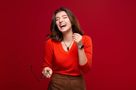 Cheerful young girl student with a smile, isolated on a red background. The concept of happiness and positiveの写真素材