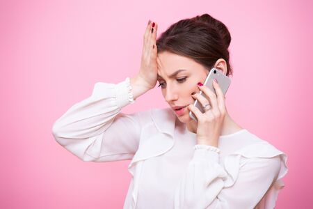 Close-up portrait of a young woman in a business suit with a mobile phone in her hands. Isolated on pink background.の写真素材