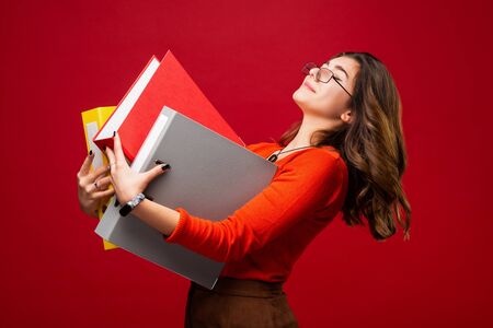The girl in glasses carries folders, with a fright on her face on a red background. Mood stress,...