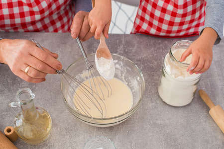 Two chefs in checkered aprons beat the egg mixture with flour in the kitchen. Cooking baked goods together. close-up.の写真素材