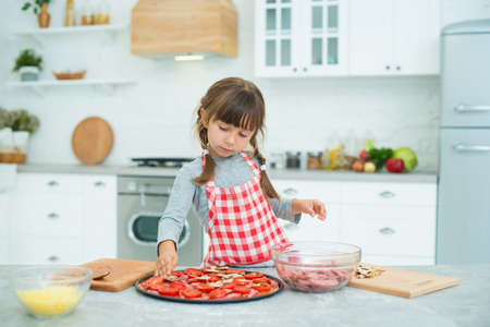 Funny girl with pigtails preparing pizza in the kitchen. Cooking class for children.の写真素材