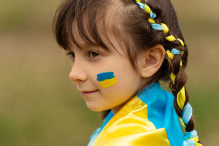 Close-up portrait of a small beautiful Ukrainian girl with two pigtails with yellow and blue ribbons like the Ukrainian flag. She asks for help to save Ukraine. stop the war. high quality photoの写真素材