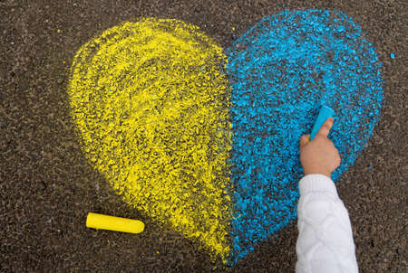 A child's hand draws a heart with crayons on the pavement with the patriotic national Ukrainian colors of yellow and blue. Stop the war in Ukraine. high quality photoの写真素材