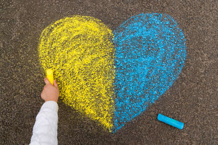A child's hand draws a heart with crayons on the pavement with the patriotic national Ukrainian colors of yellow and blue. Stop the war in Ukraine. high quality photoの写真素材