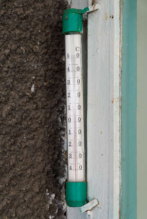 An outdoor thermometer for measuring air temperature hangs on the wall of the house near the door or...