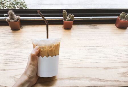 Hand holding ice coffee on wooden table backgroundの写真素材