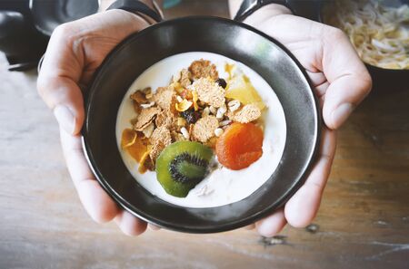 Man Holding muesli bowl, eating breakfast cereals with nuts, pumpkin seeds, oats, dried fruit and yogurt, healthy conceptの写真素材
