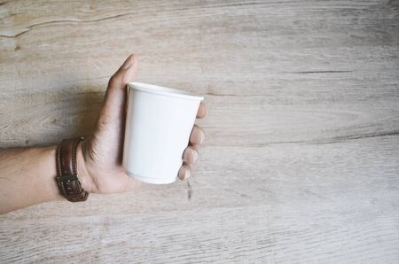 Man holding cup white paper, on wooden table, space for textの写真素材