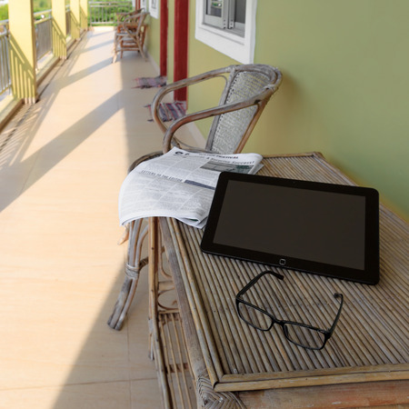 Glasses, newspaper and laptop on wooden table in guesthouse balconyの写真素材