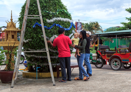SIHANOUKVILLE, CAMBODIA - DECEMBER 05,2014 Unidentified asian people hold an unidentified european caucasian girl while they happily decorate a new year tree in the street on December 05, 2014 in Sihanoukville, Cambodiaのeditorial素材