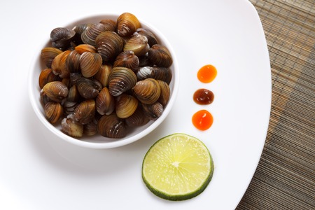 A plate with uncooked mussels and lime with sauces on a brown bamboo mat view 2