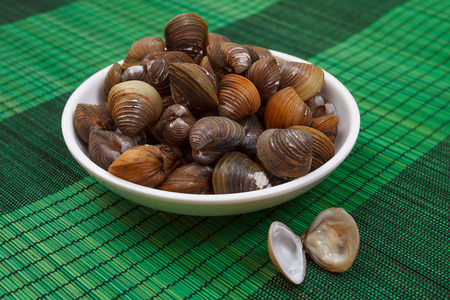 A close-up of a bowl with uncooked mussels on a green mat with one open musselの写真素材