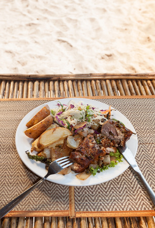 Natural light photo with shallow DOF of Cambodian barracuda steak with french fries and salad on mats on wooden table with tableware vertical view 1の写真素材