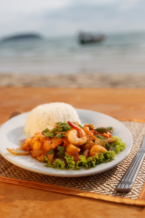 Natural light photo with shallow DOF of stewed seafood with vegetables, steamed rice with sea view backgroundの写真素材