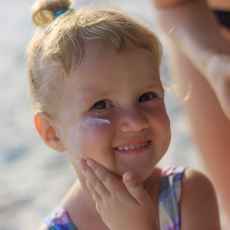 Cute baby girl applying sun screen lotion for safe tan and skin care view 2の写真素材