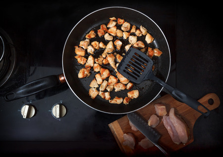 Chopped chicken fillet fried on frying pan with raw meat on board besideの写真素材