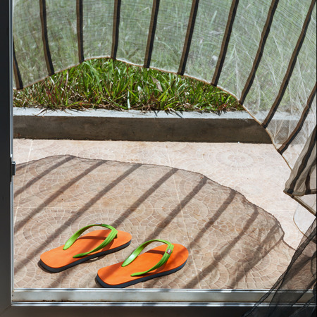 Orange flip-flops lying at a house entry with waving curtain view 2の写真素材