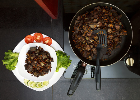 Pork liver stewed with onions and carrots and red beans in  frying pan served with vegetables on white plate view 1の写真素材