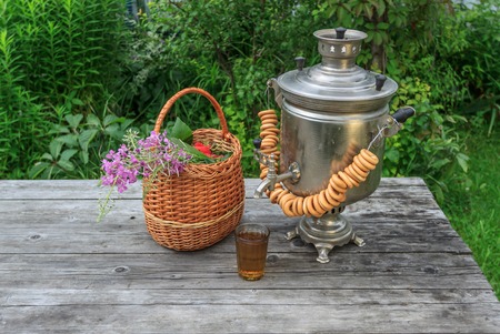 russian samovar on a rustic wooden table with berries and flowers and glass of tea in the garden front viewの写真素材