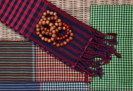 Colorful traditional khmer scarfs and buddish beads on rattan background top view closeupの写真素材