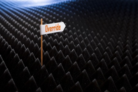 white directional sign saying OVERRIDE on bumpy black background horizontal view