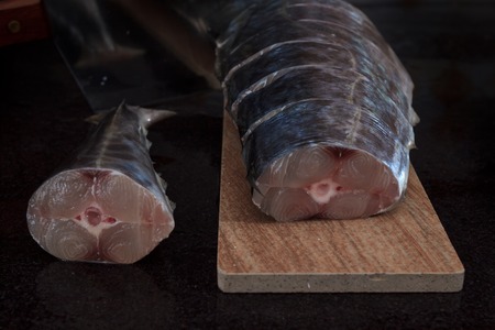 Fresh sea fish sliced and ready for cooking on wooden board  on black marble table
