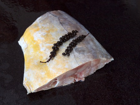 Fresh sea fish piece with green pepper on top ready for cooking on black marble table view 1の写真素材