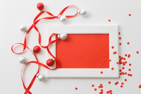 New Year and Christmas greeting card template made of white frame and red card with red ribbon, silver and red balls and red confetti, horizontal top viewの写真素材