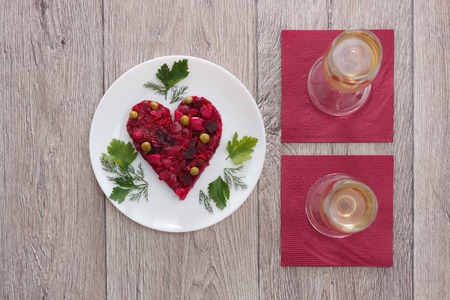 Beetroot and vegetables salad made in hearth shape served with herbs on plate with two glasses of...