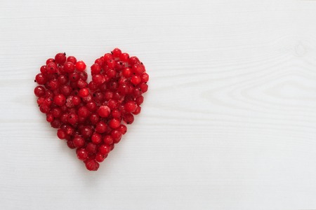 Red current berries in heart shape on wooden board with copy space, horizontal overhead viewの写真素材