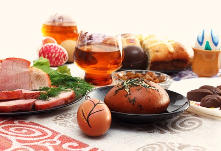 Traditional easter dinner set with sliced meat, bread with herbs, handmade colored eggs, chocolates,...