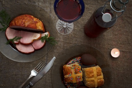 Easter dinner served on burlap tablecloth. Meat, hot cross buns, chocolate eggs and wine, horizontal top viewの写真素材